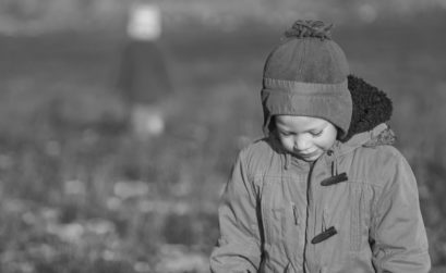 Young boy wearing a coat and woolly hat looking sad.